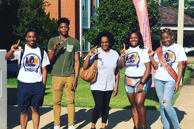 Incoming Students facing camera smiling at camera. They are wearing Lion Camp t-shirts and they have their hands in the L's up sign.