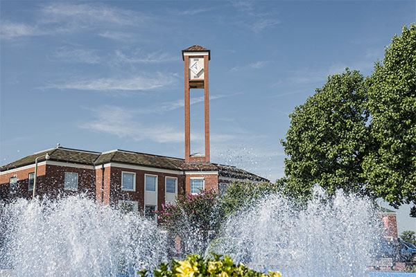 Photo facing Library on main campus with clock tower and fountain in action