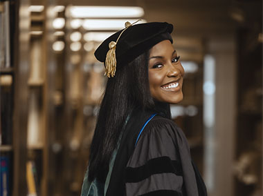 Photo of female Langston graduate in regalia looking back over her shoulder smiling