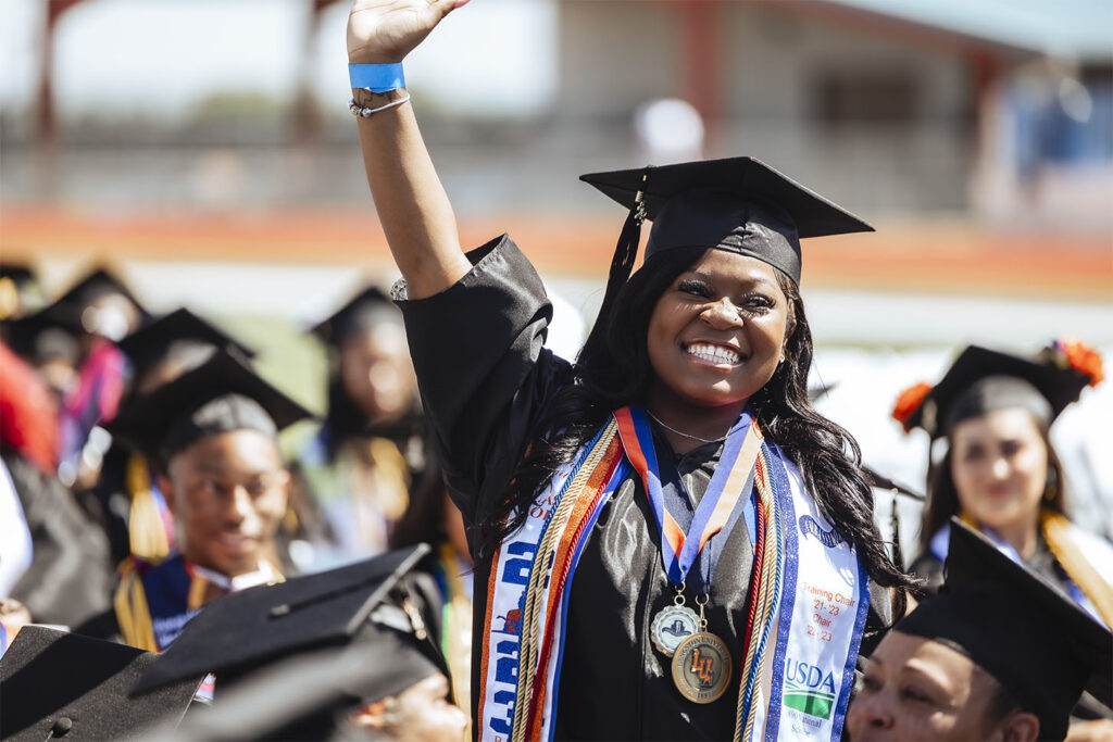 Langston graduation candidate in regalia smiling and celebrating with hand in the air
