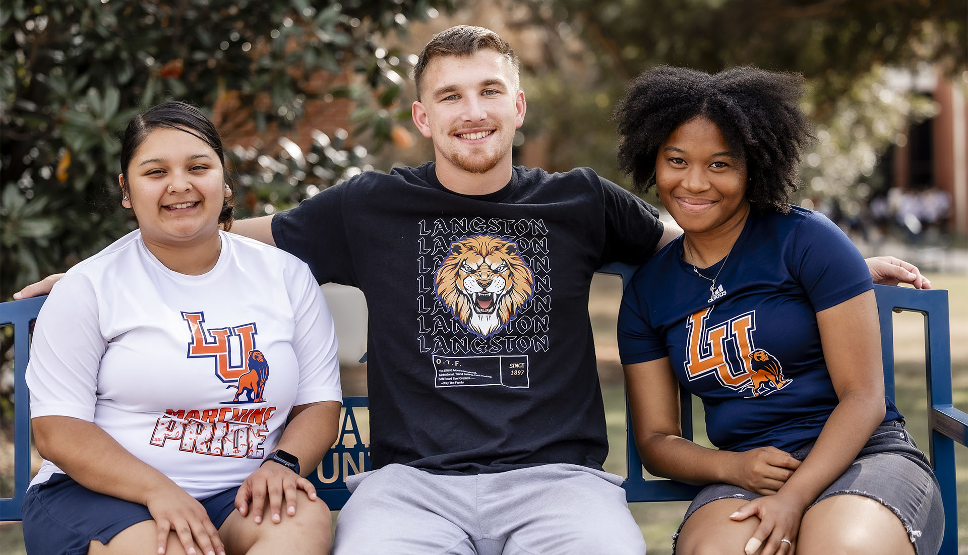 Photo of two female and one male Langston University student sitting on a bench on main campus