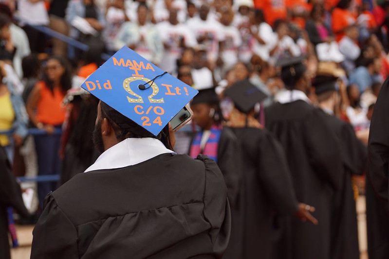 Graduate wearing cap and gown. Cap has message: Mom, I did it!