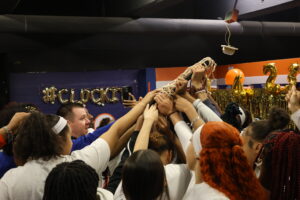 The Lady Lions place their hands on the SAC Championship trophy during their locker room huddle