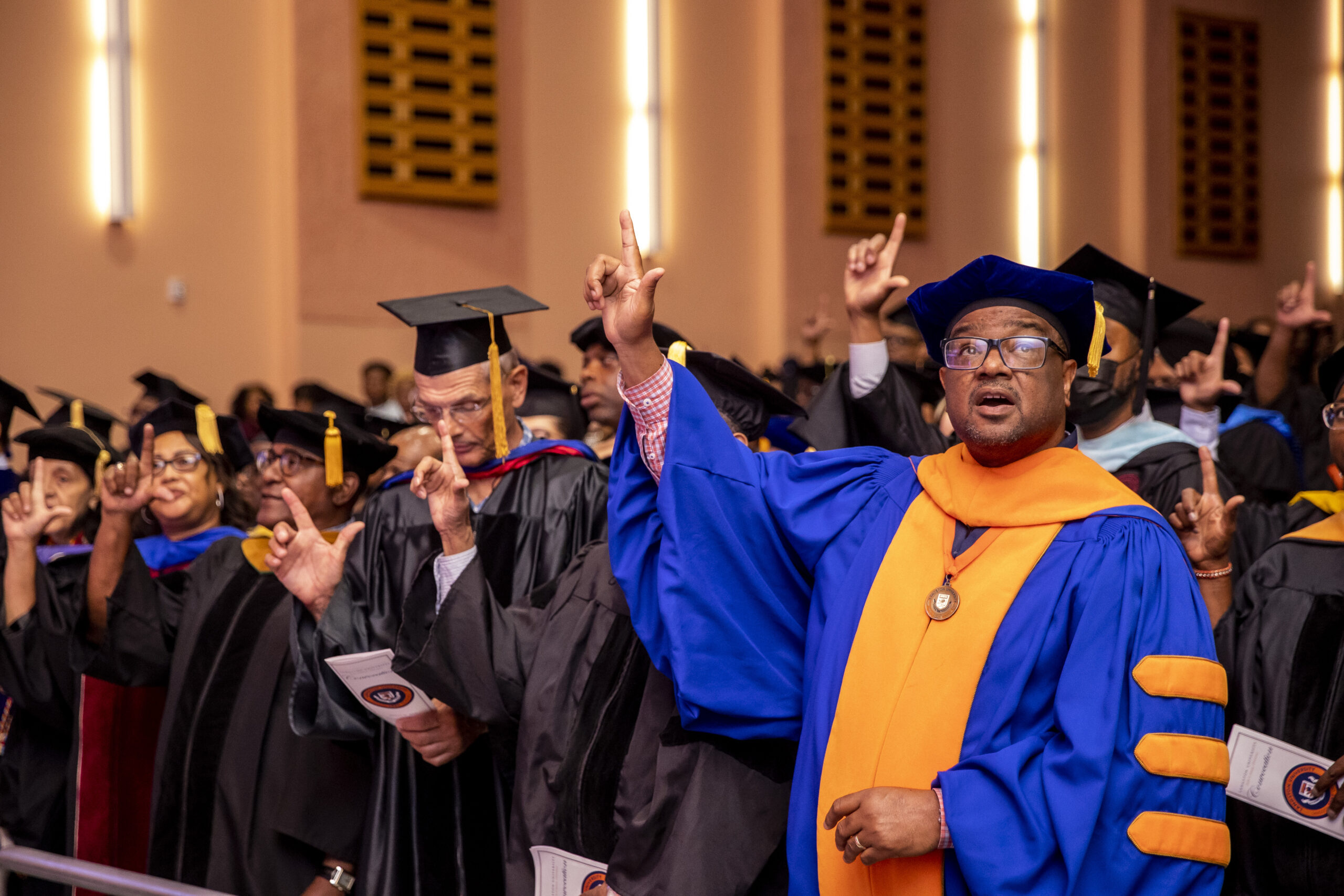faculty members in academic regalia make "L's" with their thumbs and forefingers