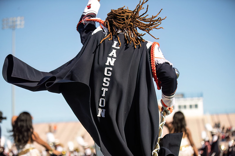 Photo taken from behind LU Marching Pride member with a cape that reads LANGSTON from top to bottom