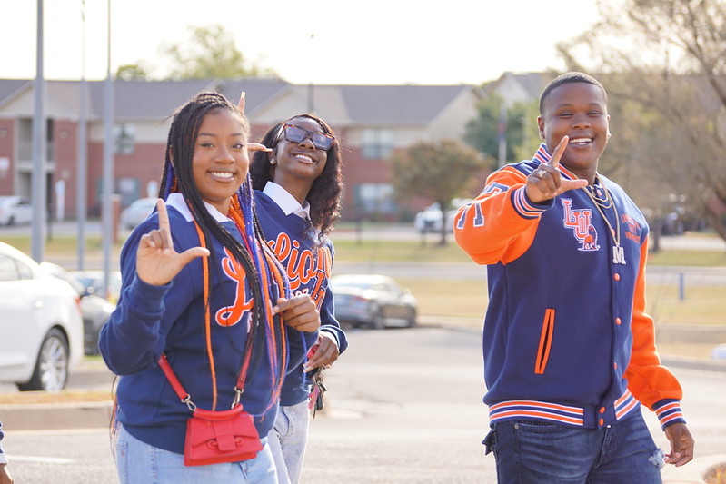 Three LU community members wearing logowear with L's up and smiling