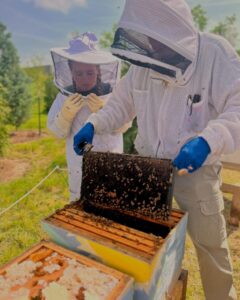 Hank Baker, in beekeeping gear, shows a student how to remove panels from a beehive. 