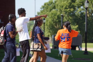a student ambassador wearing an "Ask Me" shirt gives a family directions during Lion Camp