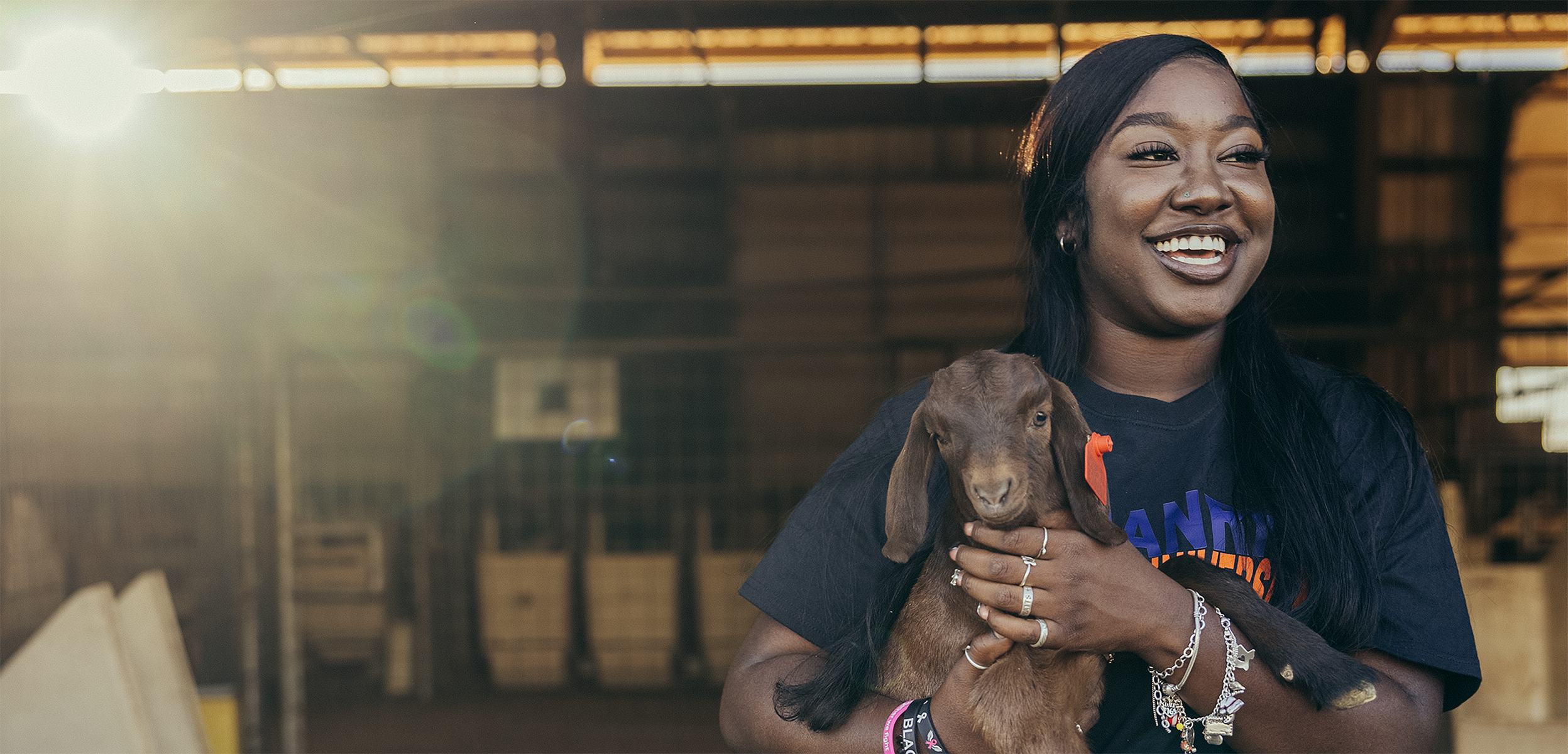 A student holding a young goat. She is smiling.