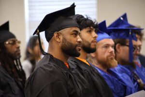Inmates in graduation caps and gowns smile as they listen to the guest speaker during the small graduation ceremony held at Dick Conner Correctional Center