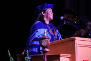 Dr. Ruth Ray Jackson dressed in blue academic regalia smiling at the podium during Opening Convocation