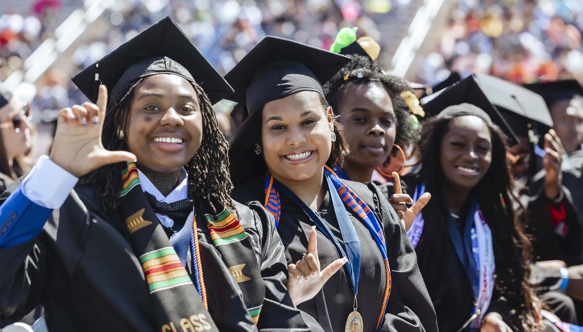 Photo of graduates in regalia at commencement seated with Ls up